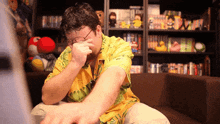 a man wearing glasses and a yellow shirt covering his face
