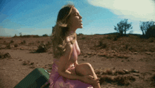 a woman in a pink dress sits on a green suitcase