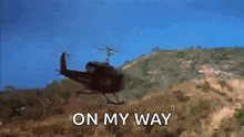 a helicopter is flying over a hill with the words on my way written on the bottom .