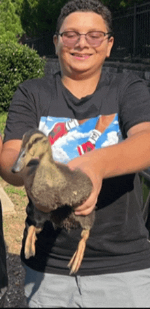 a boy wearing glasses is holding a small duck in his hands