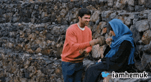 a man in an orange sweater talks to a woman in a blue headscarf