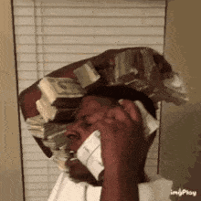 a man is talking on a cell phone while wearing a stack of money on his head .