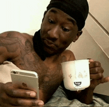 a shirtless man is holding a cup of tea and a cell phone