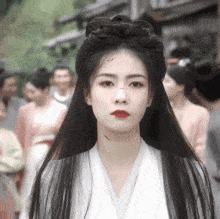 a woman with long black hair and red lips is standing in front of a crowd .
