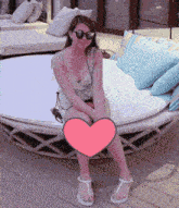 a woman wearing sunglasses sits on a round bed with a pink heart in front of her