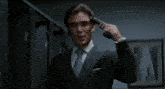 a man in a suit and tie is holding a gun to his head in the fog .