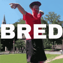 a man in a red shirt stands in front of a sign that says bred