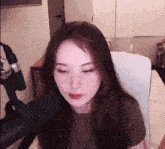 a woman is sitting in a chair in front of a microphone and looking at the camera .