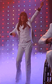 a woman in a white suit is dancing on a stage in front of a man in a wheelchair .