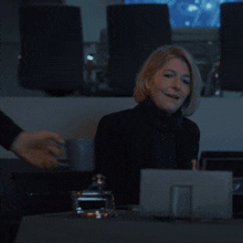 a woman in a black turtleneck sits in front of a computer