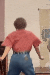 a woman in a red shirt and blue jeans is dancing in a living room .