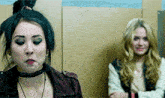 two women are standing next to each other in a room and one is wearing a choker .