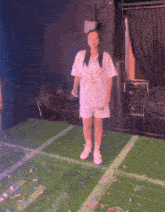 a girl in a white shirt and shorts is standing on a stage surrounded by confetti and fans .