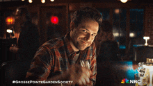 a man in a plaid shirt is sitting at a bar with nbc written on the bottom right