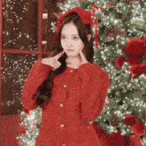 a woman in a red sweater is standing in front of a christmas tree and making a funny face