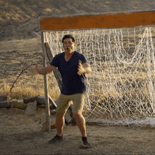 a man in a blue shirt and khaki shorts stands in front of a soccer net