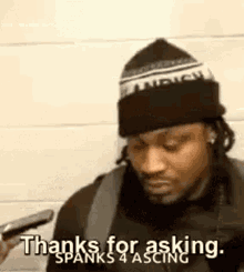 a man wearing a hat is holding a cell phone and saying `` thanks for asking spanks 4 ascing '' .