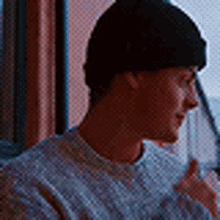 a man wearing a beanie is sitting in front of a window and looking out .