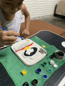 a young boy is painting a piece of clay with the word happy