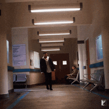 a man walking down a hallway with a sign on the wall that says ' waiting room ' on it