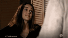 a woman in a black shirt is standing in front of a window with shutters and the hashtag #theblacklist