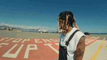 a man with dreadlocks stands on a runway with a stop sign in the background