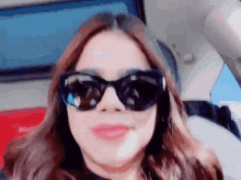 a woman wearing sunglasses is sitting in a car and smiling