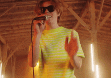 a young man is singing into a microphone while wearing sunglasses .