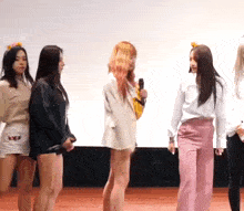 a group of women are standing next to each other on a stage and one woman is holding a microphone .