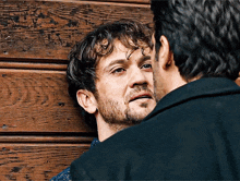 a man with a beard is leaning against another man 's wall