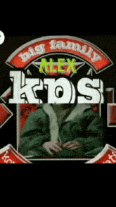 a man in a green jacket sits in front of a sign that says alex kos