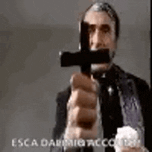 a man in a suit and tie is pointing a gun at a cross .
