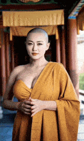 a woman with a shaved head and a very large breast is wearing a yellow robe