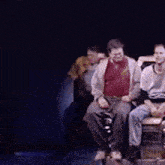 a man in a red shirt is sitting on a stage with other people