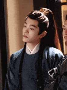 a man with a ponytail and braids is wearing a blue shirt
