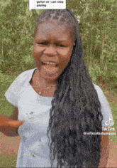 a woman with braids is standing in front of trees and a sign that says guitar so i can stop saying on it
