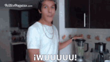 a man in a white shirt is standing in front of a blender and says " wuuuuu "