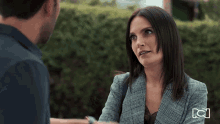 a woman in a plaid jacket is talking to a man in a black shirt