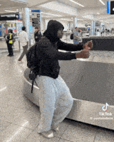 a man in a black hoodie is standing on a conveyor belt at an airport