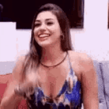 a woman is sitting on a couch smiling and waving her hand .