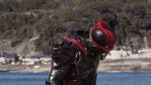 a person in a black and red costume is standing in front of the ocean