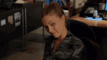 a woman in a camouflage shirt is sitting in an office