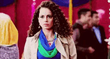 a woman with curly hair is wearing a blue and green scarf and a white jacket .