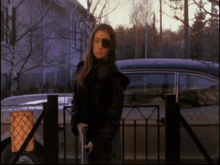 a woman with an eye patch stands in front of a fence and a car