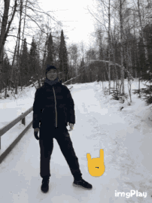 a man in a black jacket stands in the snow next to a yellow sign that says heavy metal