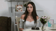 a woman is sitting at a table with a vase of flowers