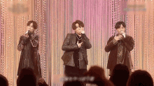 three men are singing into microphones in front of a crowd of people .