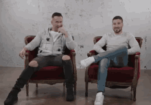 two men are sitting in chairs with their legs crossed and one is laughing