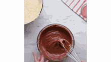 a person is whisking a bowl of chocolate frosting .