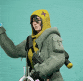 a woman in a green jacket with a yellow cross on her hood is holding a beaker